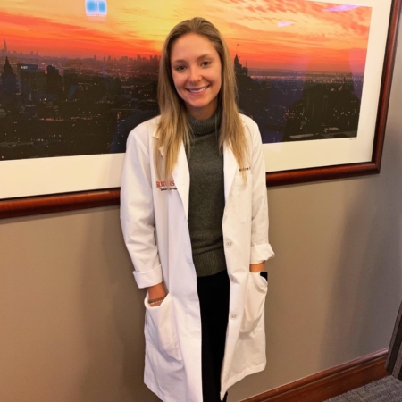 Josie Dudznik in lab coat against a wall